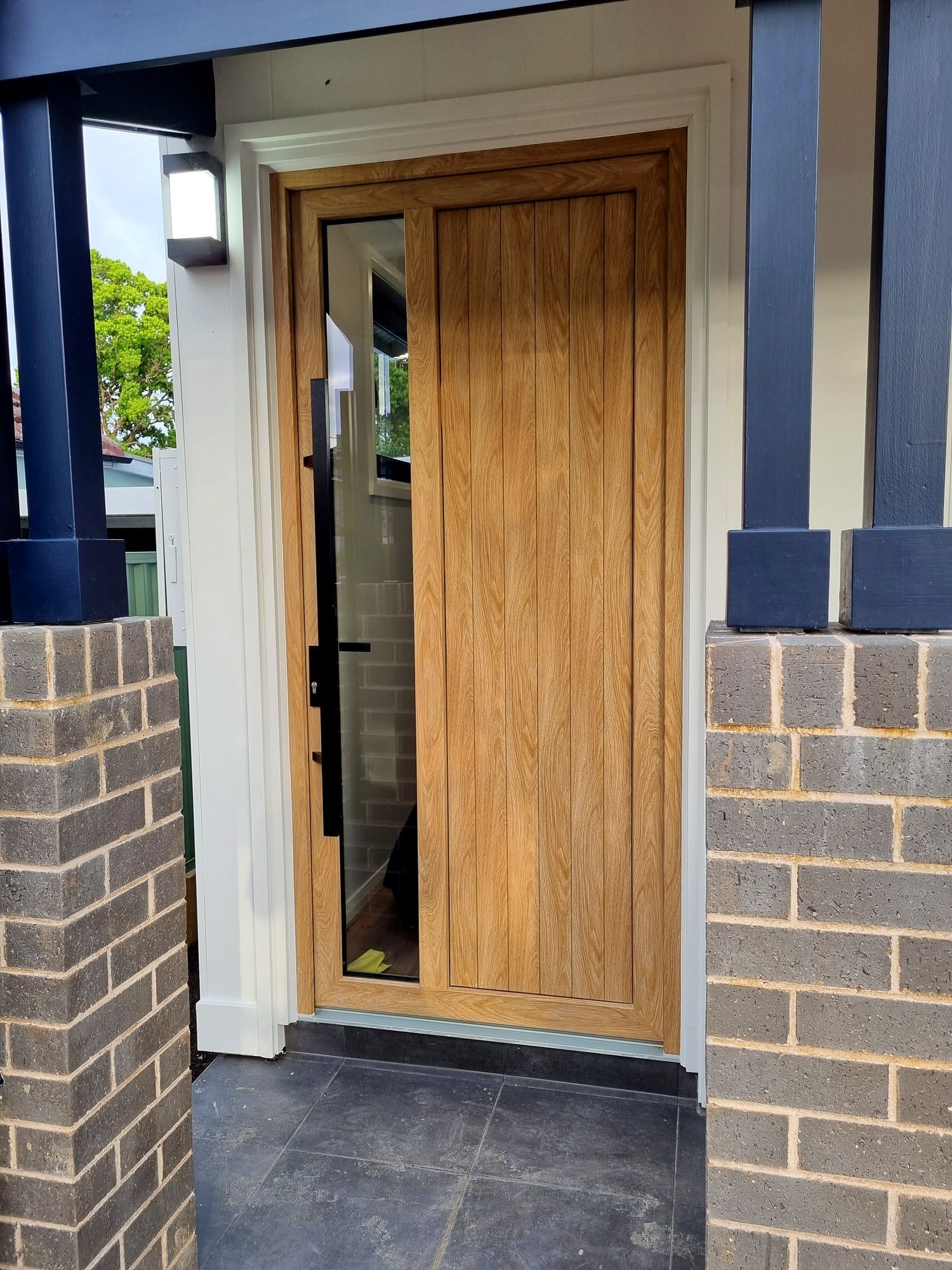 Timber entry door with a glazed sidelight, framed by brick piers and a charcoal portico