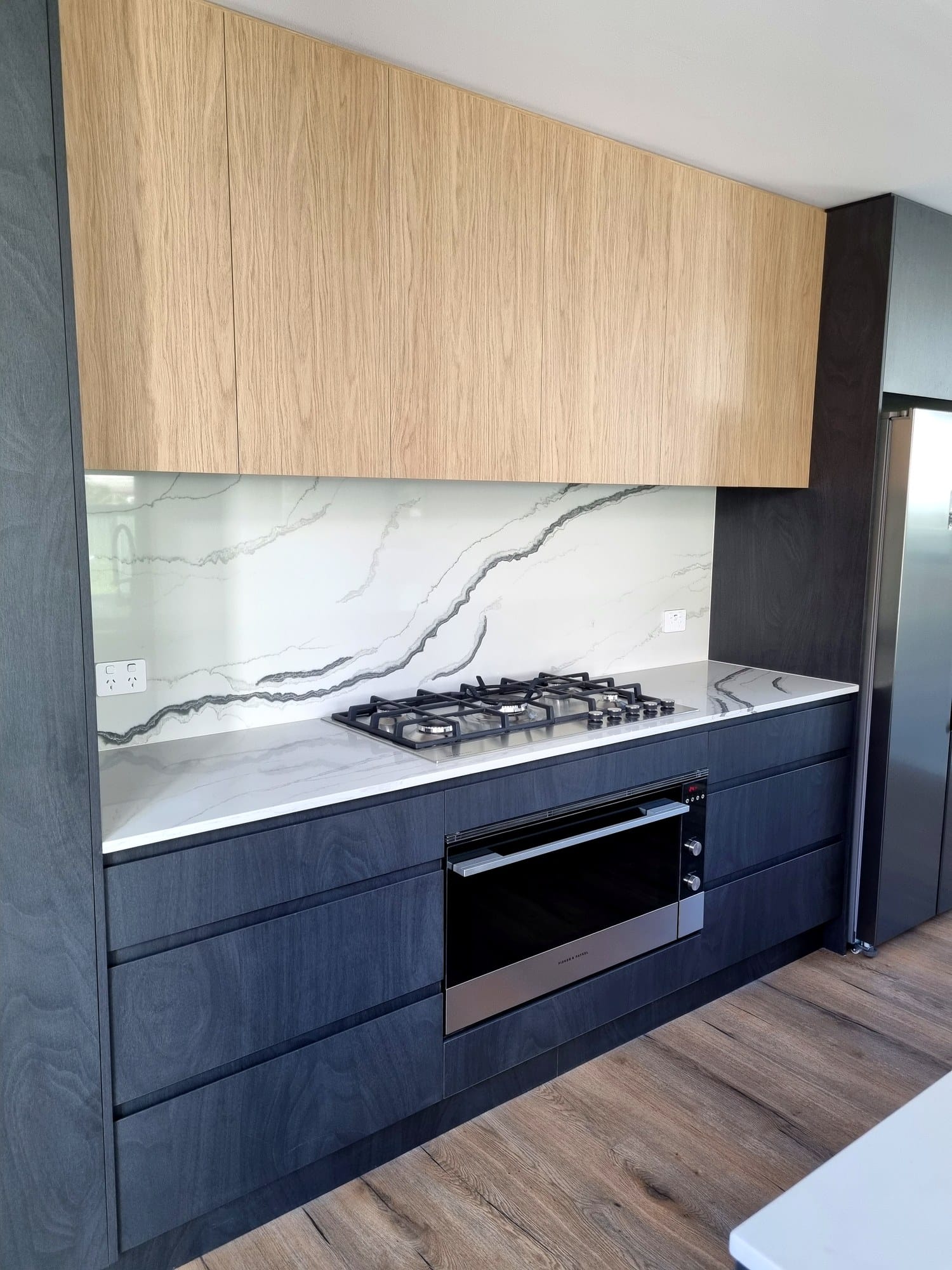 Kitchen detail with a marble-look stone splashback, gas cooktop and dark timber joinery beneath oak cabinets