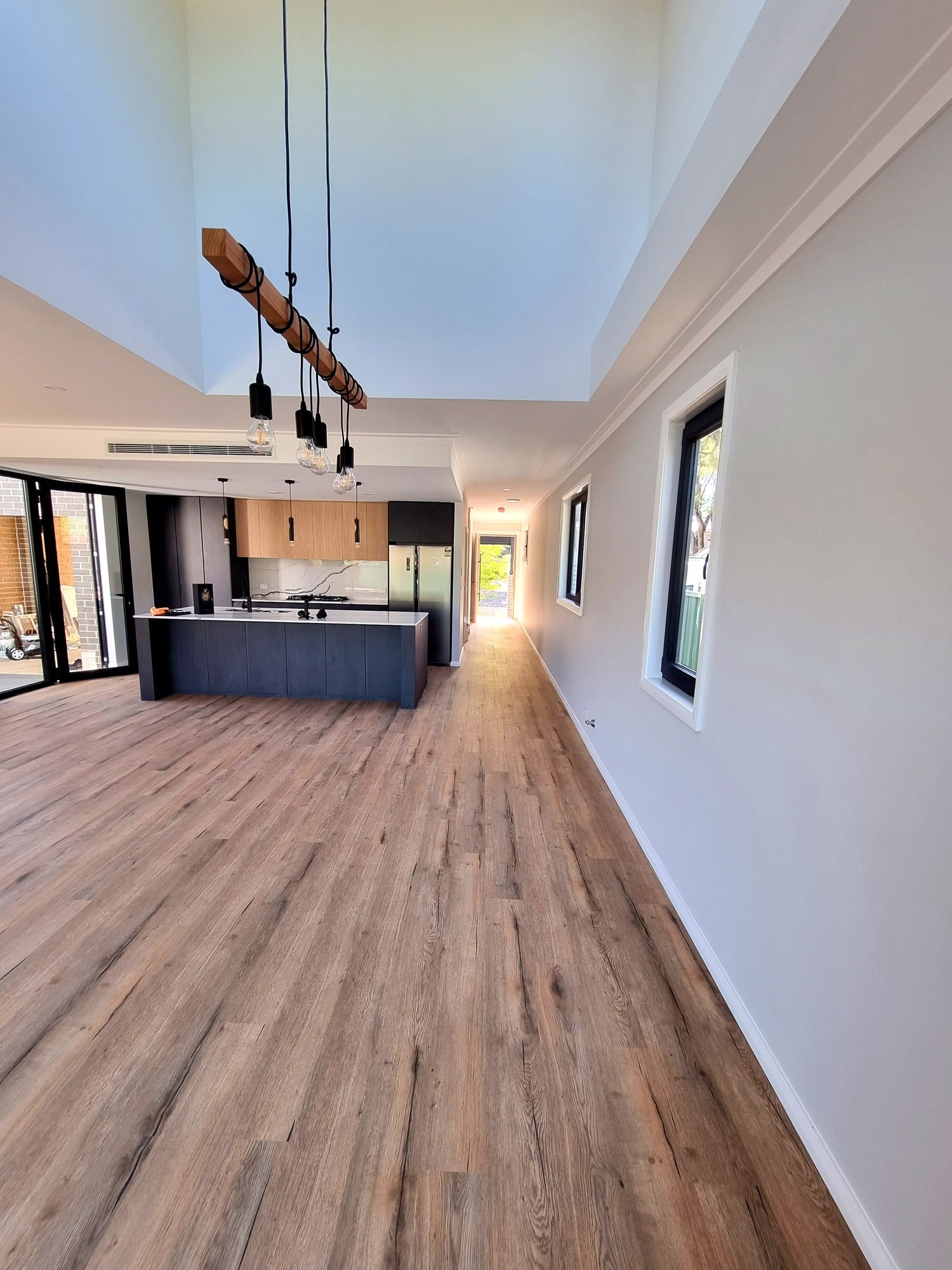 Double-height void over the living spine, drawing light down to the kitchen and timber floors