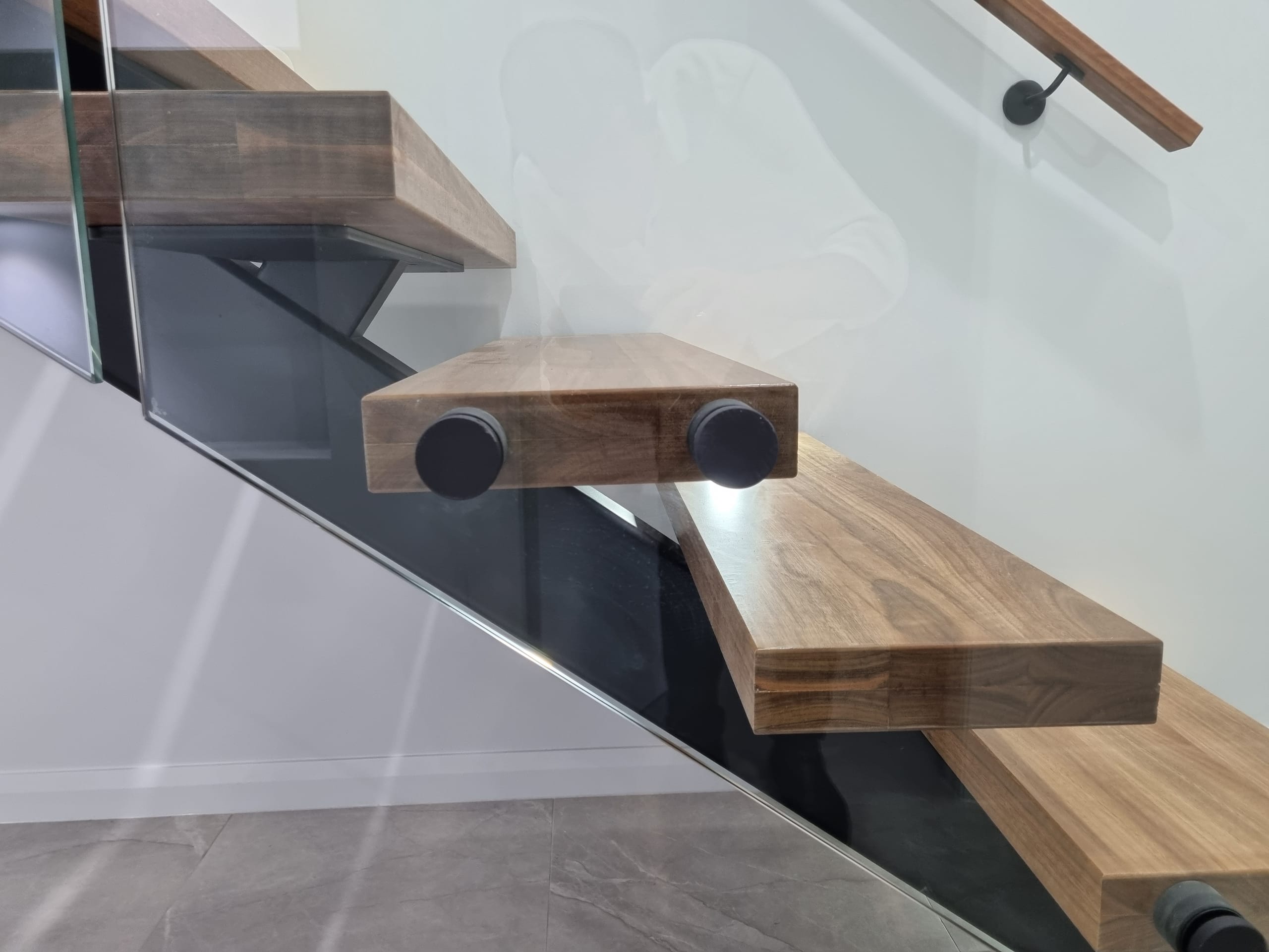 Detail of the floating timber treads cantilevered off a black steel spine behind a glass balustrade