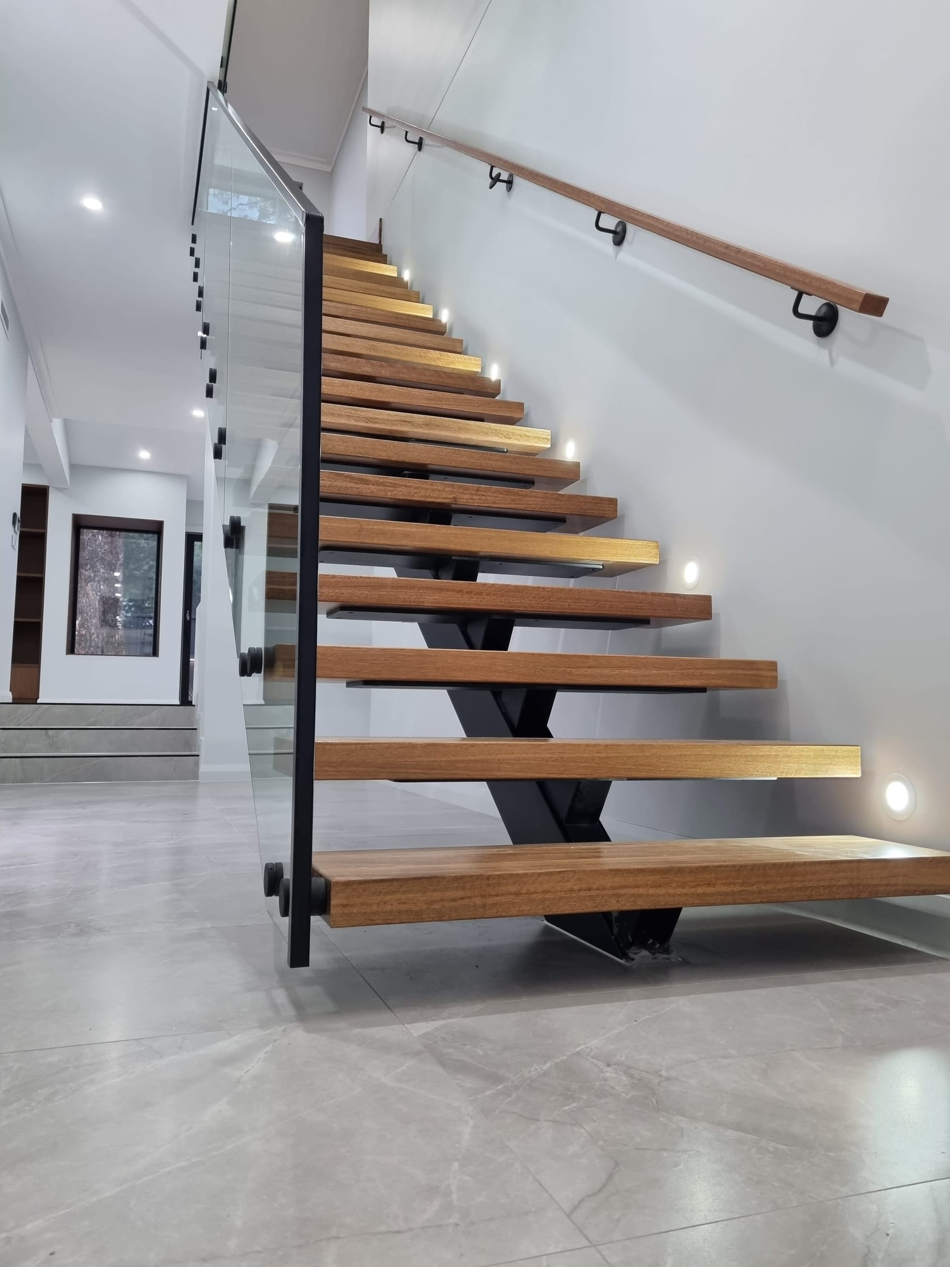 Floating timber staircase with a black stringer, glass balustrade and a timber wall-mounted handrail