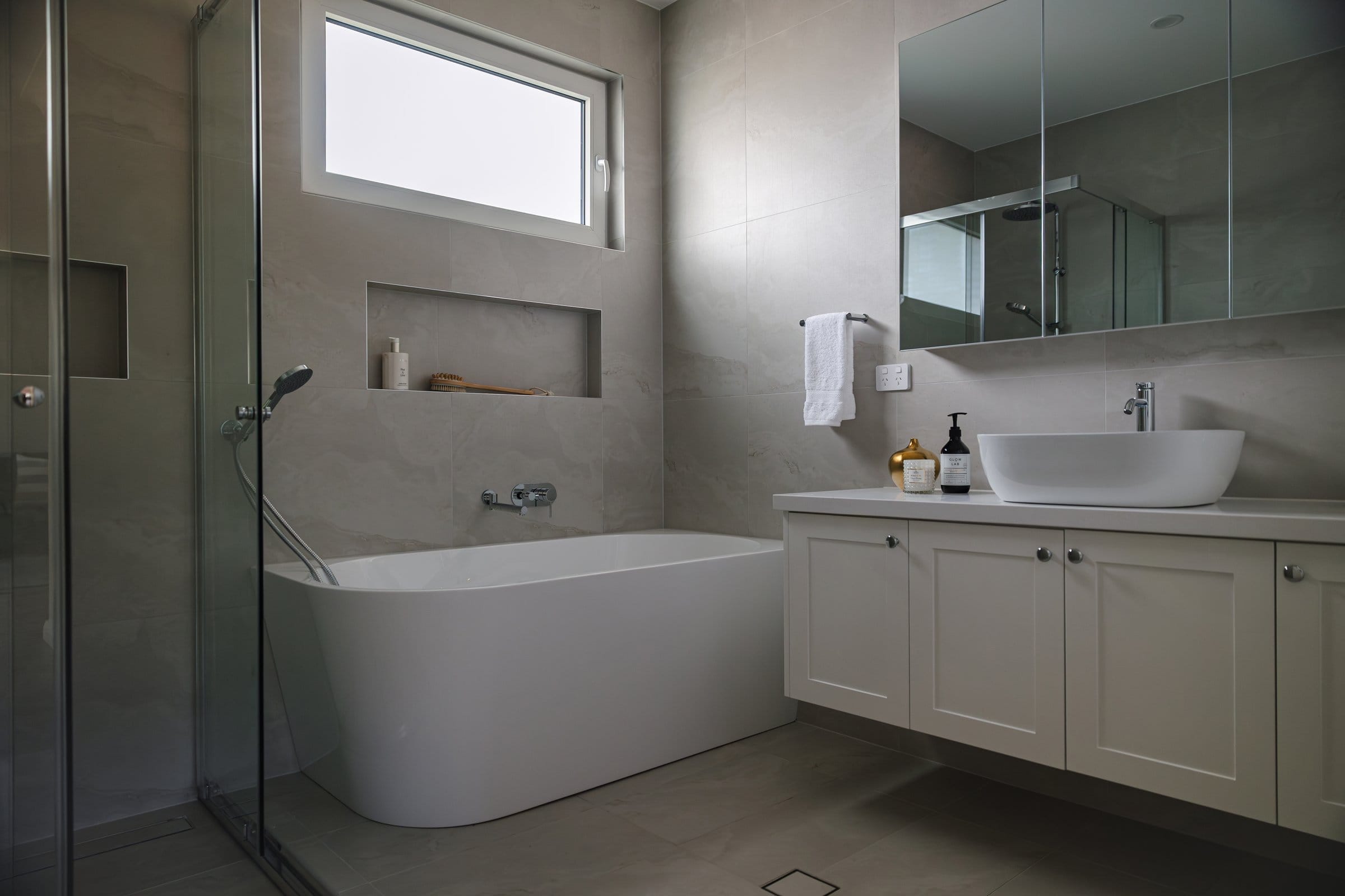 Stone-tiled bathroom with a freestanding tub, walk-in shower and a vessel basin on a shaker vanity