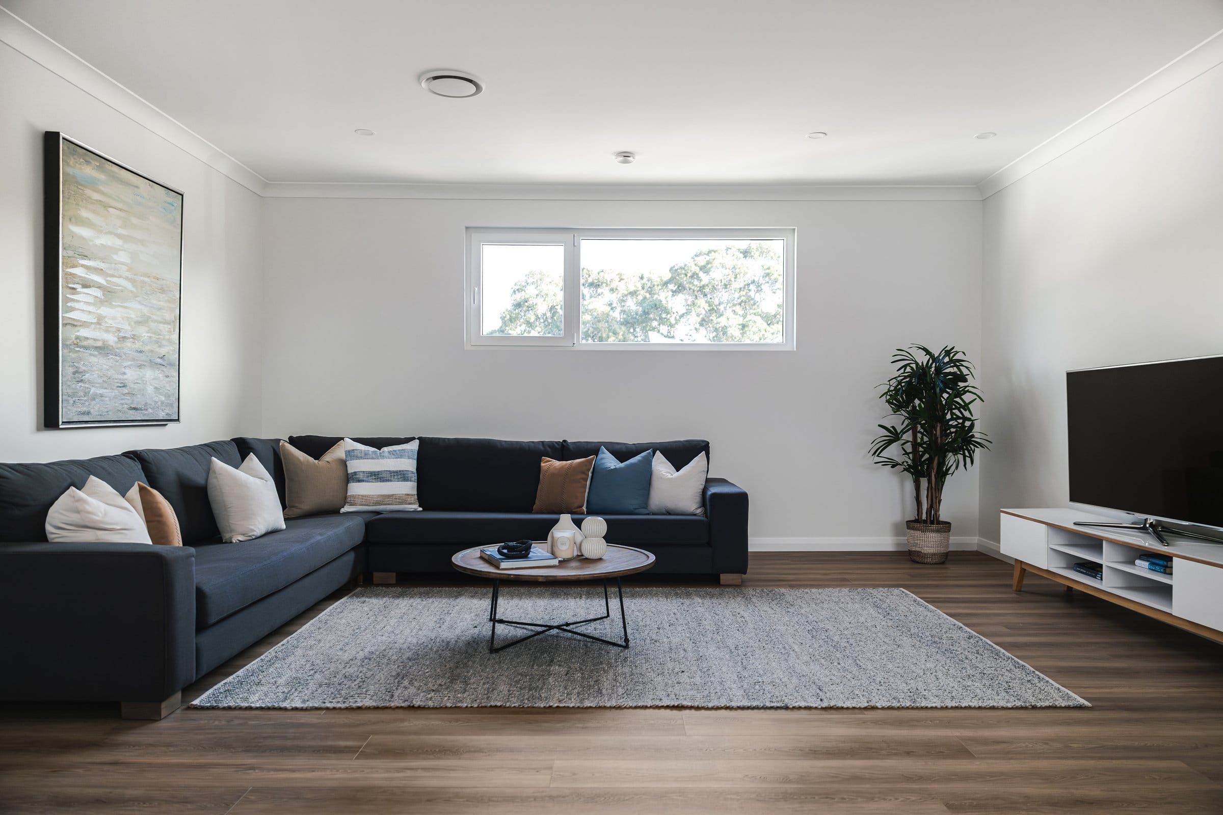 Casual rumpus with a navy L-shaped sofa, timber floors and a leafy garden outlook