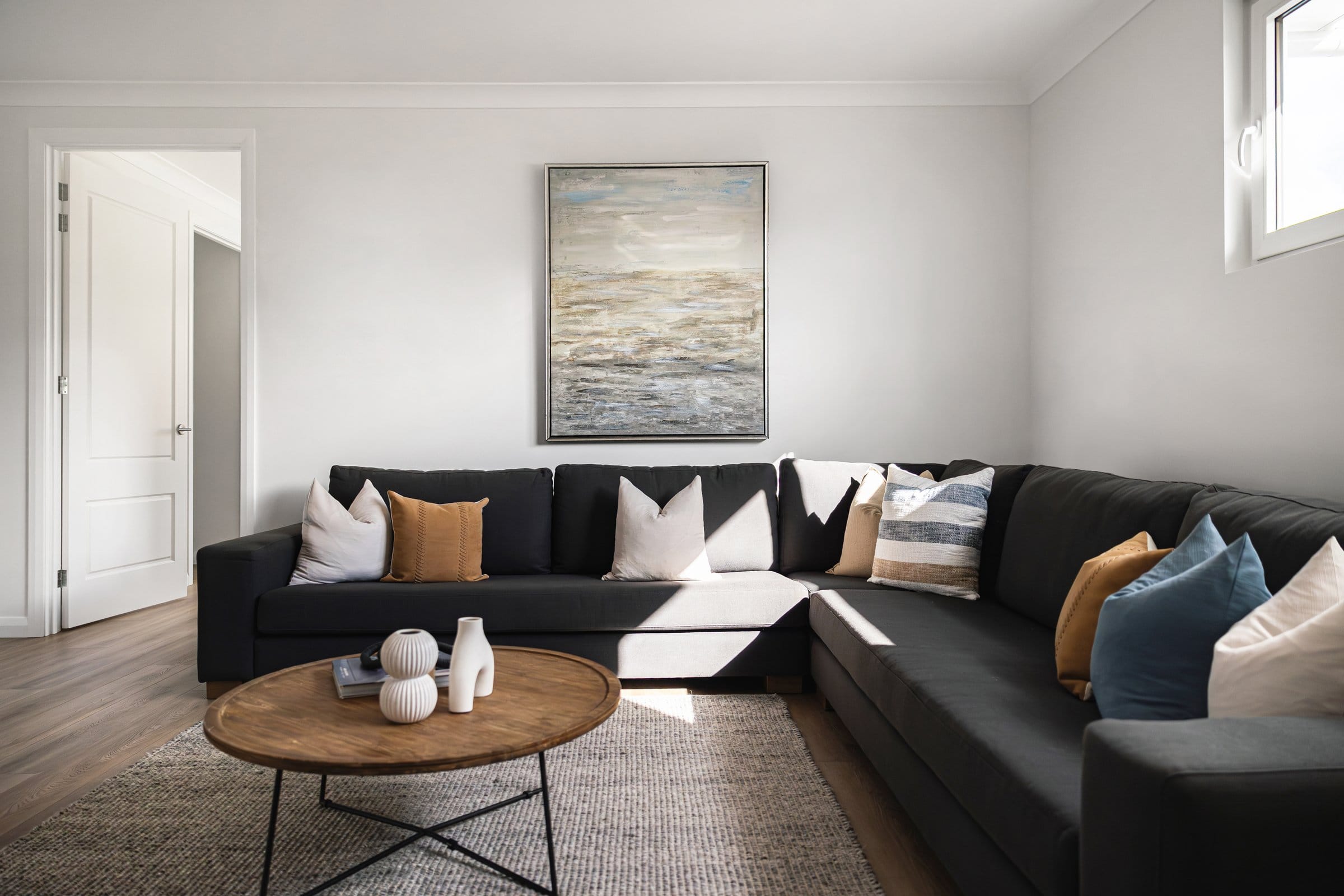 Second living area with a charcoal sofa, a round timber coffee table and abstract artwork
