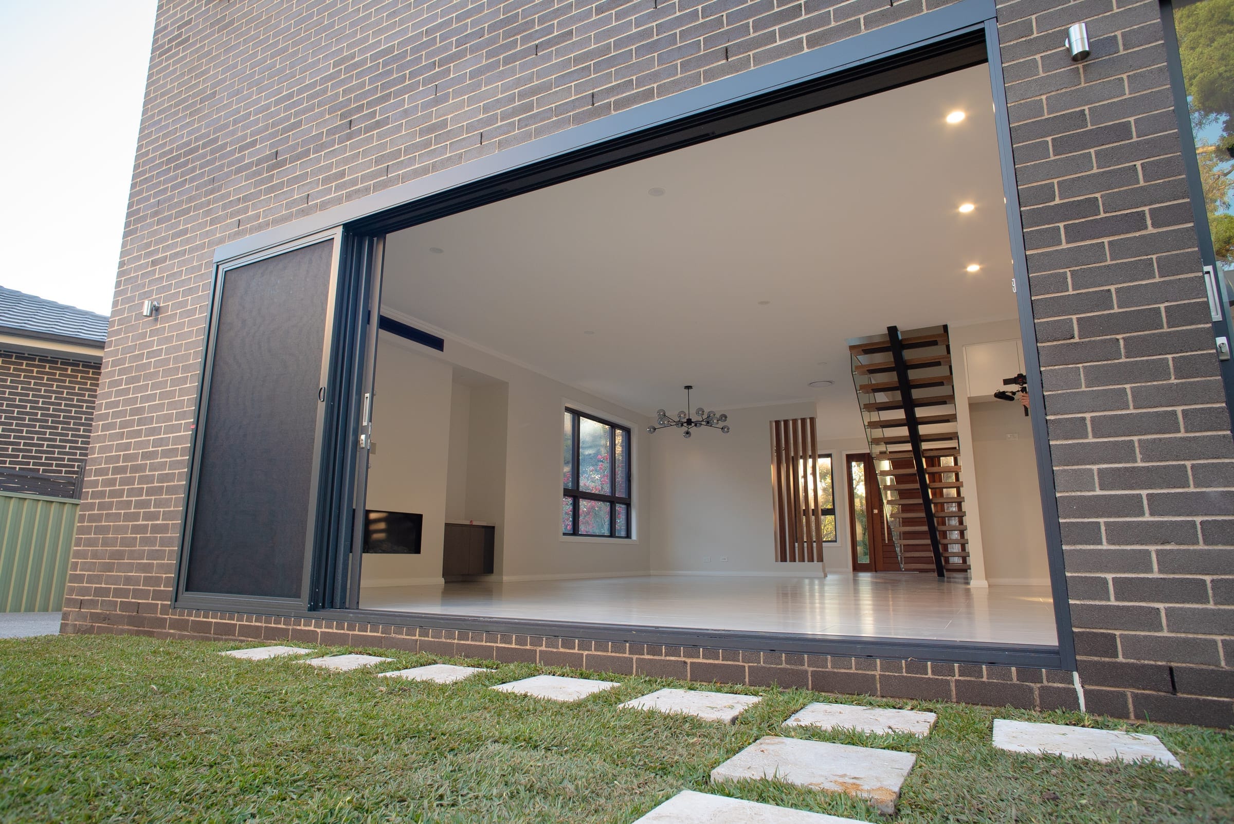 Wide aluminium stacker doors opening the living level to the rear yard with a stepping-stone path across the lawn