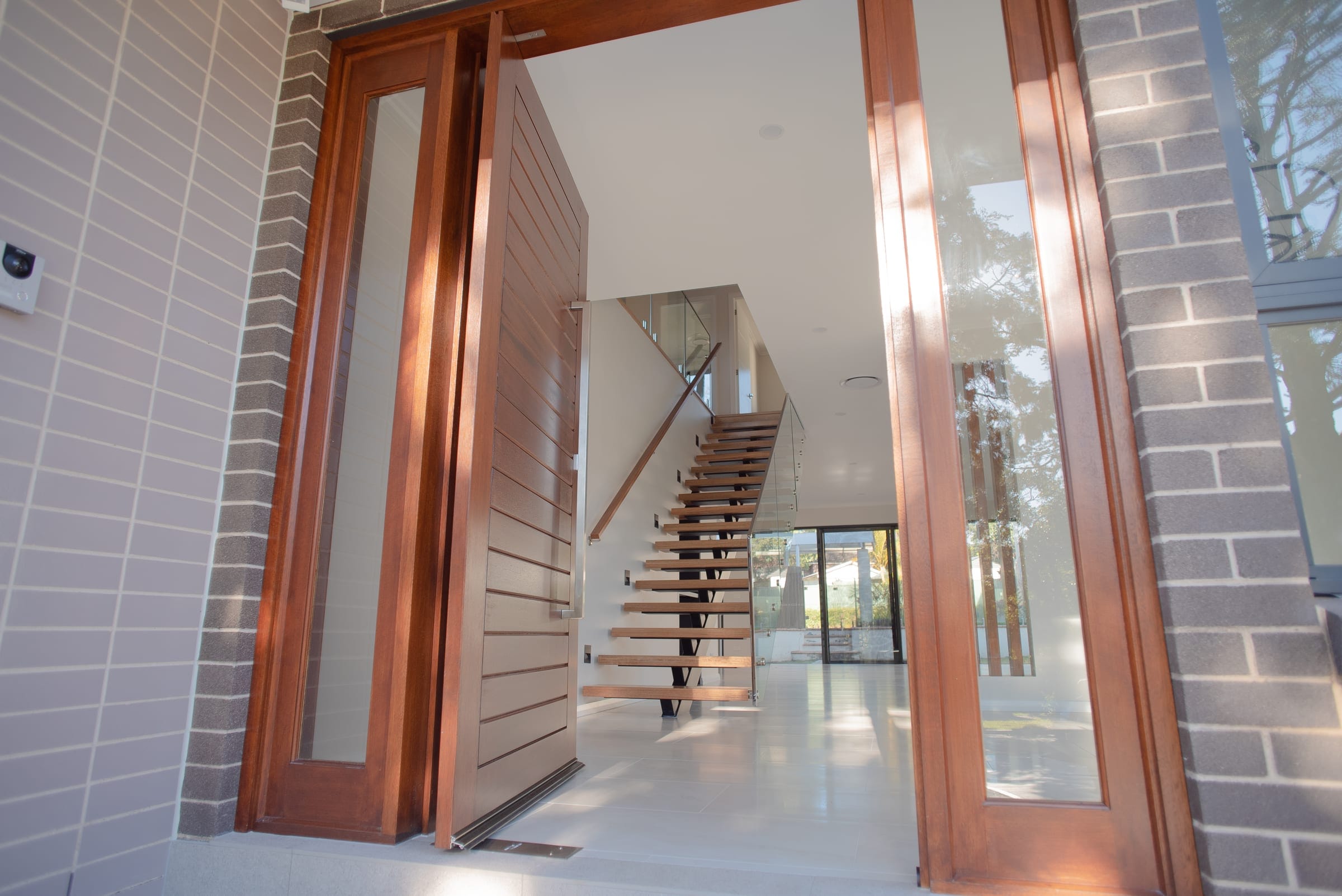 Timber pivot entry door open to a view of the floating staircase beyond