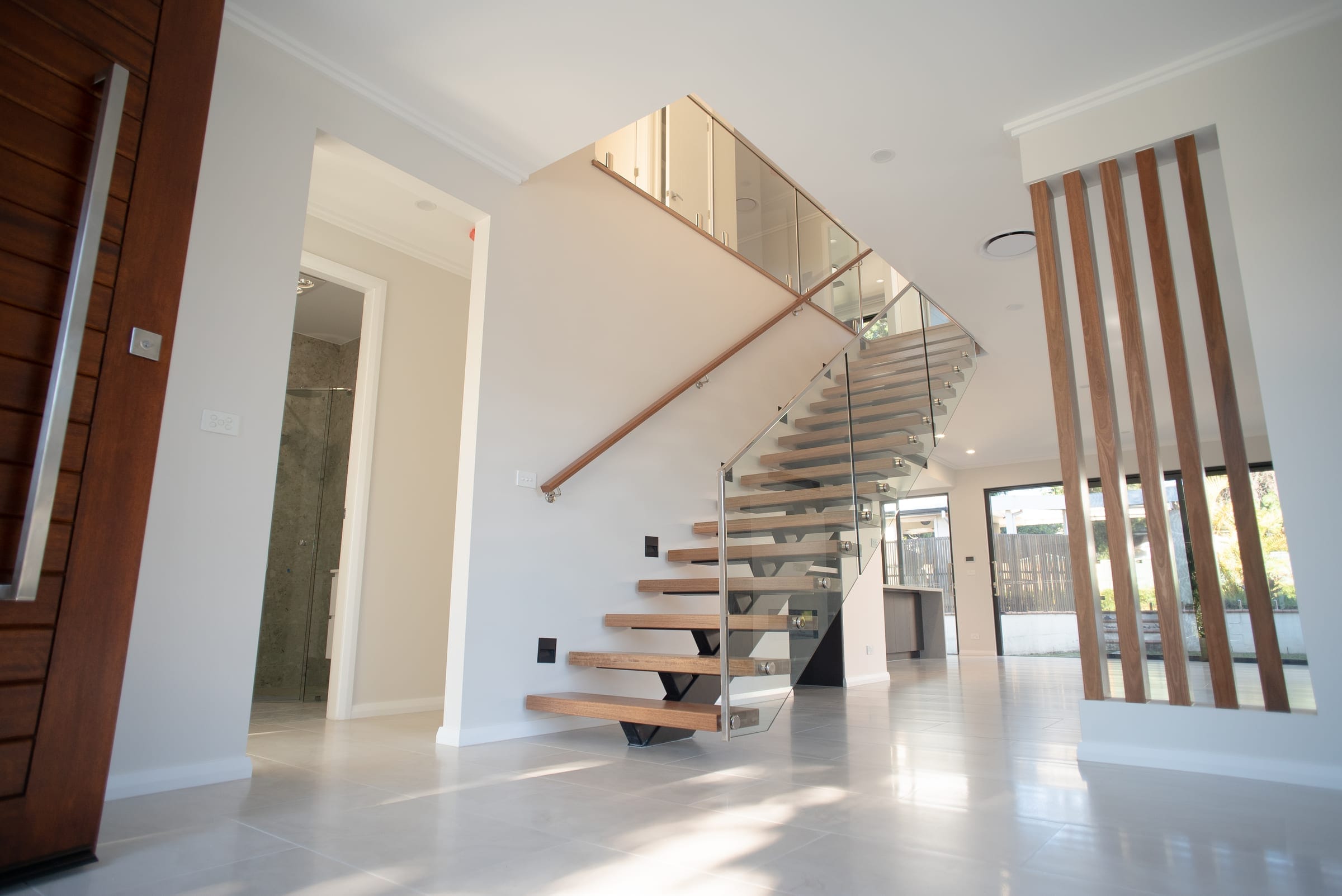 Floating timber staircase with a glass balustrade and timber handrail, opening to the living level and tiled floors