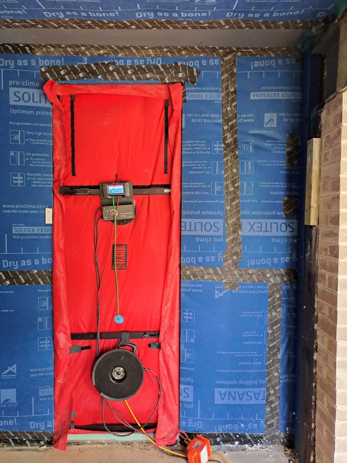 Blower-door fan rigged in a doorway against the airtightness membrane, mid-build, on a Marvel Homes site