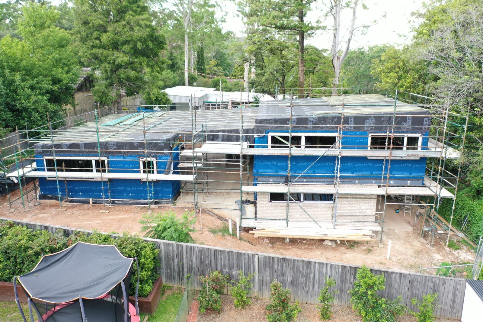 Aerial view of a Marvel Homes passive house under construction, wrapped in airtight membrane, scaffolding up