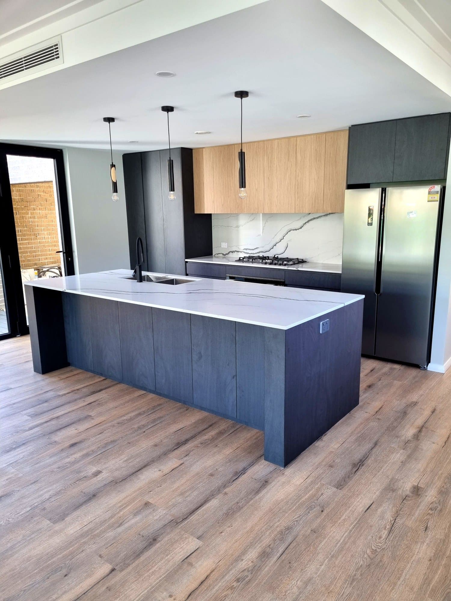 Stone waterfall island with black tapware, a marble-look splashback and oak upper cabinetry