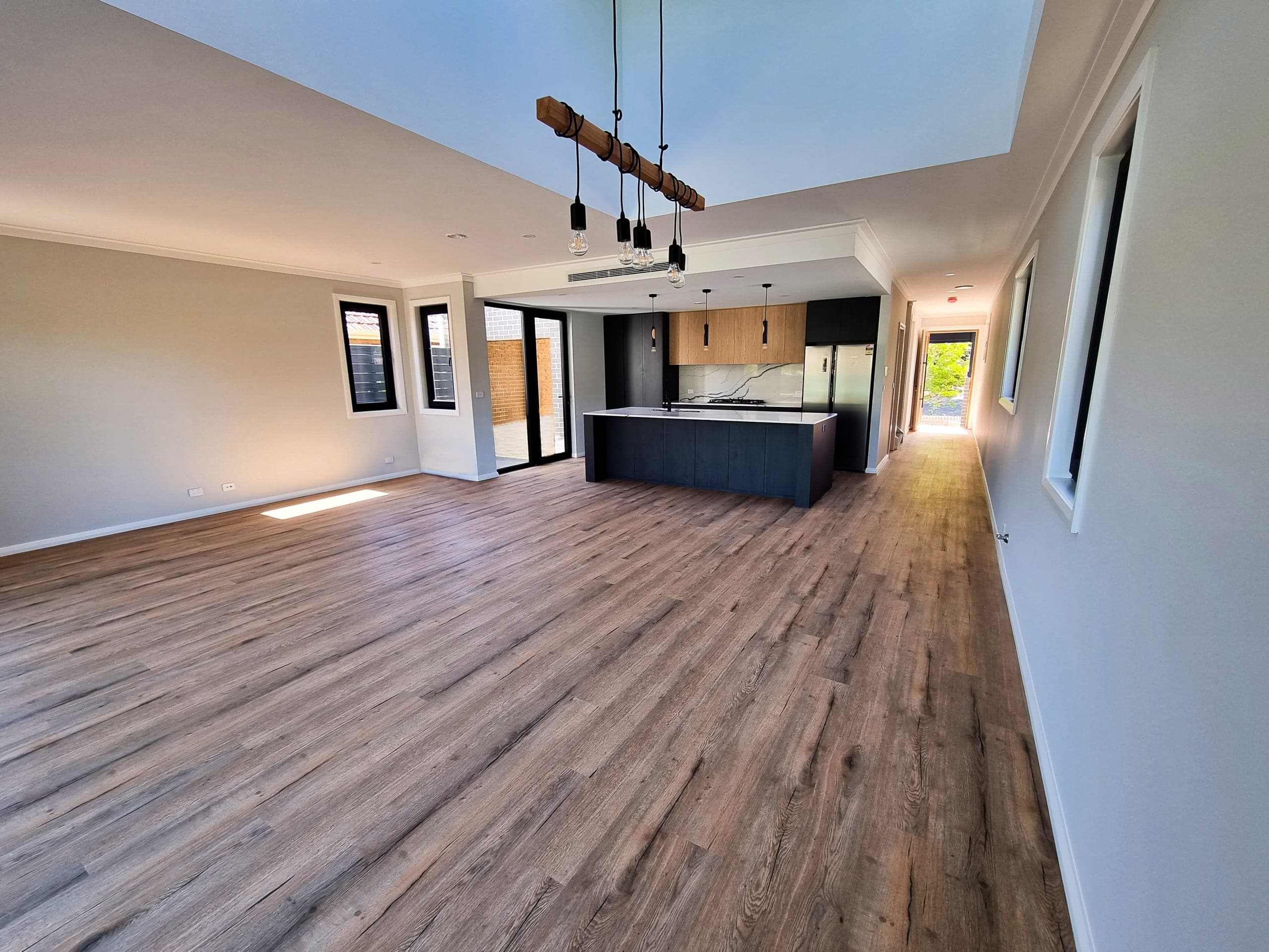 Open-plan living, dining and kitchen in oak-look flooring, with a dark timber island and a feature timber beam pendant