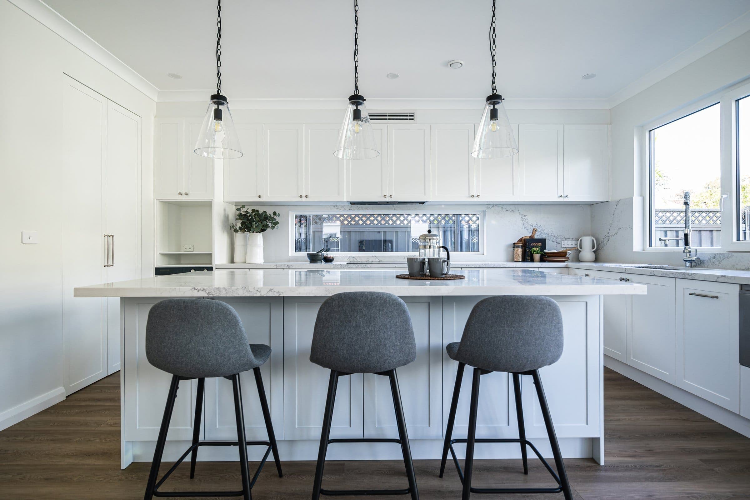 Shaker kitchen with a marble-look stone island, glass pendant lights and grey bar stools